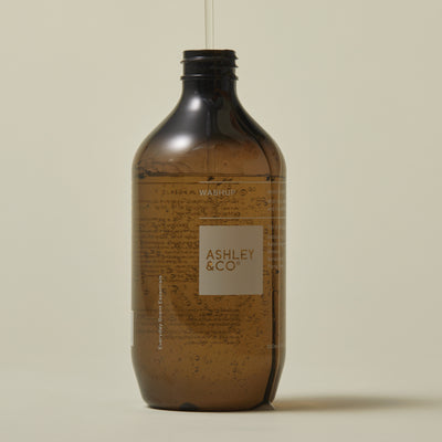 An amber glass bottle with a black cap and a white label reading 'ASHLEY & CO' on a warm beige background.